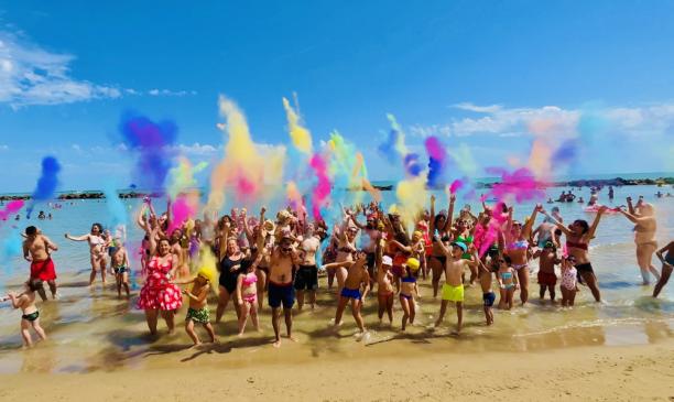 Gruppo festeggia in spiaggia con polveri colorate.